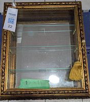 Top view of gold framed curio cabinet showing glass shelves and measurement tag 17x14 inches