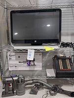 Photo showing HP all-in-one monitor on a wire shelf, Dyson vacuum box below, and vintage adding machine to the side.