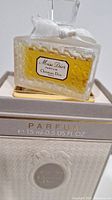 Close-up of Miss Dior Parfum glass bottle with label and amber perfume liquid inside, displayed on box.