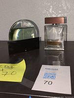 Two perfume bottles: Mont Blanc Presence (curved metallic design) on left, Dolce & Gabbana The One (rectangular glass bottle with wooden cap) on right, both used and partially full or empty.