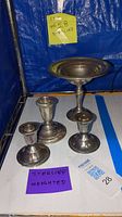 Four sterling silver pieces including three weighted candle holders and one compote on display against a blue background with labels indicating sterling silver and weighted.