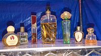 Perfume bottles on a metal rack with a blue backdrop, viewed from the front showing labels and general shape and design of each bottle.