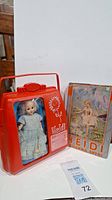 Vintage Heidi doll in a red plastic pocketbook case standing next to the original Heidi book by Johanna Spyri.