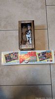 View of the boxed Chris Bassitt "Hound on the Mound" bobblehead along with the closed and sealed 1991 Donruss Baseball Puzzle and Cards box on a tiled floor.