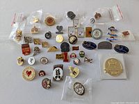 Multiple vintage enamel pins laid out on white surface. Pins include sports teams, commemorative events, and national themes.