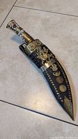 Photo of full Gurkha Khukuri in black leather sheath with detailed brass embellishments and studs.