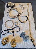 Overview photo of all jewelry pieces on white textured paper background, showing various earrings, bracelets and a necklace