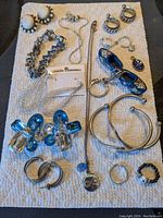 Full assortment of vintage and costume jewelry laid out on a white textured cloth with multiple earrings, rings, bracelets, necklaces, and a decorative shoe charm.
