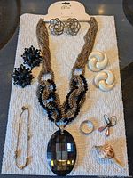 Full view of jewelry items laid on a white textured cloth showing the necklace, earrings, rings, and pins.