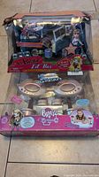 Photo showing Lil' Bratz Lil' Bus in box with doll Ailani, and i-Bratz lip-shaped speakers in separate box beneath it.