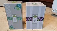 Boxes of two Scentsy products: Scentsy Go Solid White and Scentsy Lumina seen standing upright on floor.