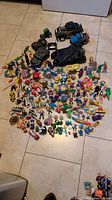 Wide assortment of vintage toys laid out on floor including action figures and vehicles