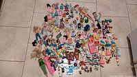 Overview of many small vintage dolls, action figures, small toys, and figures scattered on tile floor.