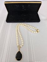 Full view of the pearl necklace with black teardrop pendant laid inside an open black velvet presentation box.
