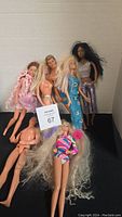 Lot of 7 Barbie dolls displayed standing and lying down showing variety of outfits and hair styles