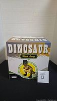 Photo of the front of the dinosaur table lamp box showing the product name and image of the lamp.