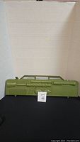 Green plastic carrying case for army men shaped like a military weapon, front view showing handle and damage