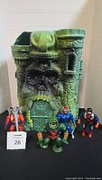 Full view of Castle Grayskull playset with four He-Man action figures in front, showing scale and detail.