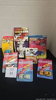 Multiple vintage toy cars, sealed in their original blister card packaging, displayed together showing front view of cards with graphics and cars inside.