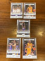 Front side of five 2010 Panini Kobe Bryant basketball cards in protective sleeves showing different action shots from NBA games with Lakers purple and gold colors.
