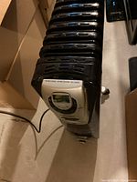 Top angled view of the DeLonghi heater showing fins and silver digital control panel with display screen.