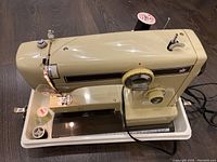 Full side view of beige Eaton Viking EZ28 sewing machine in white plastic carry case with spool of thread installed.