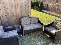 Full view of the 3-piece outdoor patio set on grass next to wooden fence and house side. Set includes two single chairs and one love seat with visible cushions.