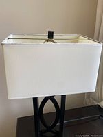 Close-up showing the white rectangular fabric lampshade and part of the black metal base with intersecting oval design.