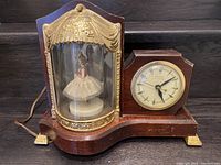 Full view of the illuminated musical dancing ballerina clock showing the ballerina under glass dome and the clock face on the walnut base with gilded feet and trim.