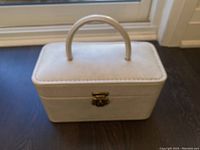 Closed white leather train case with brass clasp and top handle shown from front