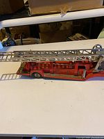 Side view of vintage pressed steel toy fire truck showing long extendable ladder and detailed body.