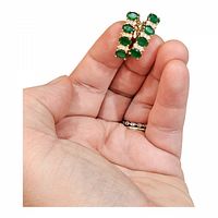 Photo showing pair of gold-tone hoop earrings with oval green stones and clear accent stones held in hand