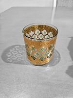 Top angle photo showing the cup's gold filigree and green diamond pattern on clear glass base.