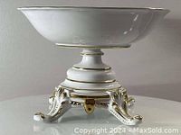 Side view of white porcelain footed fruit bowl with gold decorative accents and ornamented legs base.