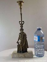 Full view of the antique solid bronze candle holder next to a water bottle for scale, showing bronze figure and marble base.