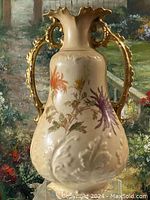 Front view of antique vase showing intricate floral hand-painted design and textured cream base with gold handles.