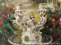 Full view of the porcelain double candle holder with two candle cups and central figurine among floral decorations.