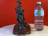 Front view of bronze-colored cowboy figurine on horse next to a water bottle for size reference.