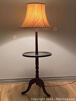 Full view of the heritage floor lamp illuminated, showing the mahogany wood stand, green leather round table top, and fabric lamp shade.