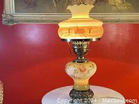 Front view of the hand painted hurricane glass table lamp showing floral painted glass base and frosted glass shade with ruffled edge.