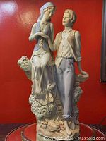 Front view of the porcelain figurine showing the man standing holding a basket behind his back and the woman seated on a rock with flowers.