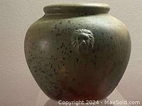 Full view of round pottery vase with speckled glaze and lion head sculpture on front.