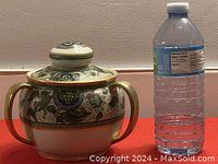 Hand-painted Nippon porcelain jar with lid and two gold-colored handles, shown next to a water bottle for scale.