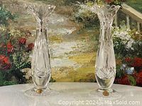 Two clear crystal candle holders with scalloped tops on a white surface with floral background.