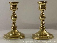 Front view of two polished solid brass candlesticks showing turned design and octagonal bases.