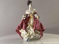 Front view of Royal Doulton figurine depicting a woman in a red and cream Victorian style dress.