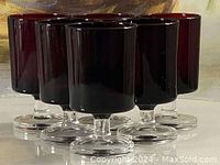 Close-up of five ruby red Luminarc Cavalier wine glasses showing the thickness of the glass, color intensity, and foot design.