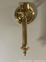 Full view of the solid brass wall candle sconce mounted on the wall showing the full length and reflective polished finish.