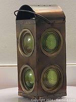 Front and side view showing the copper oil lamp shaped like a traffic signal light with green circular lenses, handle on top, and aged patina.