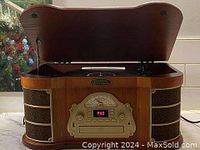 Front view of the turntable phonograph with lid open showing turntable area inside and ornate brass front panel with speakers on sides